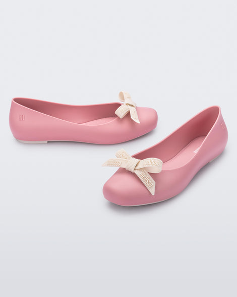 Angled view of Melissa Aura flats in pink with  beige bow details on a light gray background