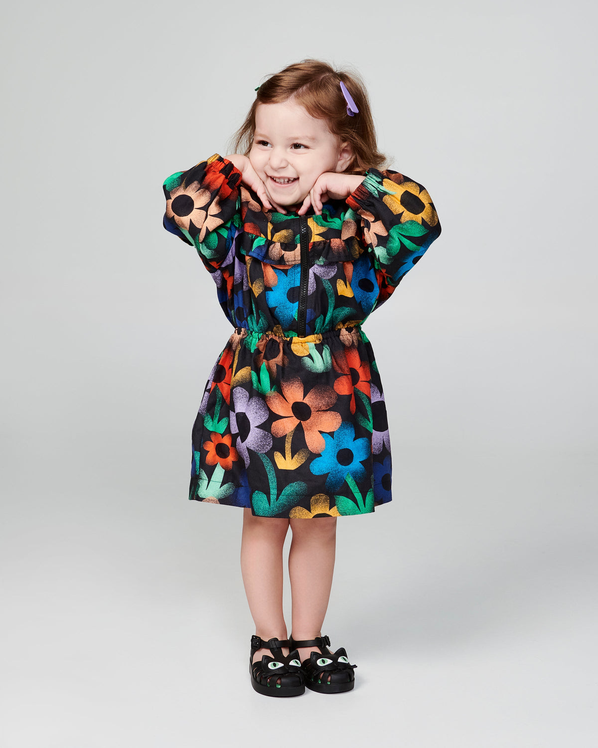 Child model in a black floral print dress wearing a pair of black baby Possession Cat sandals
