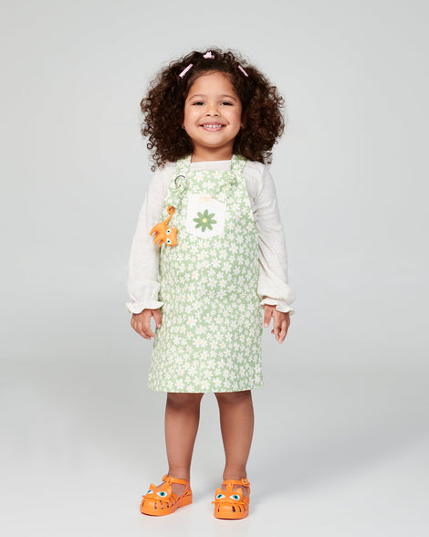 Child model in a green floral dress wearing a pair of orange baby Possession Cat sandals