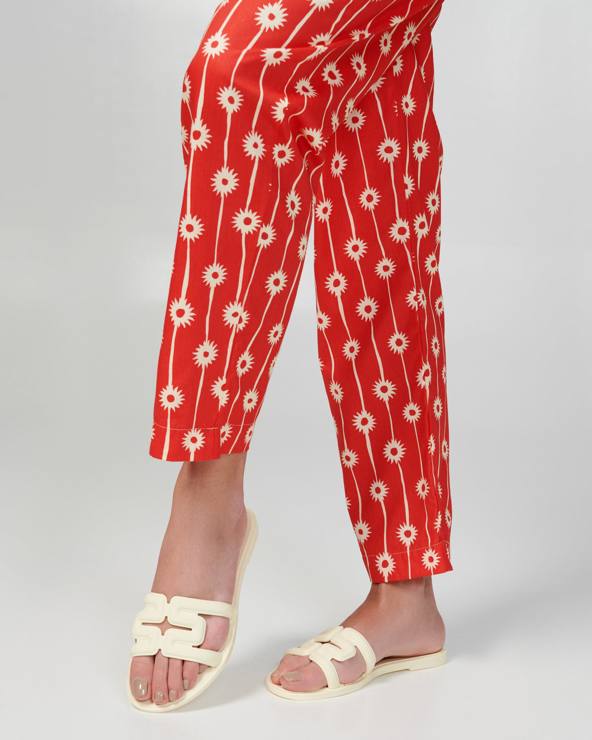 Model's legs in red pants wearing a pair of beige M Slides.
