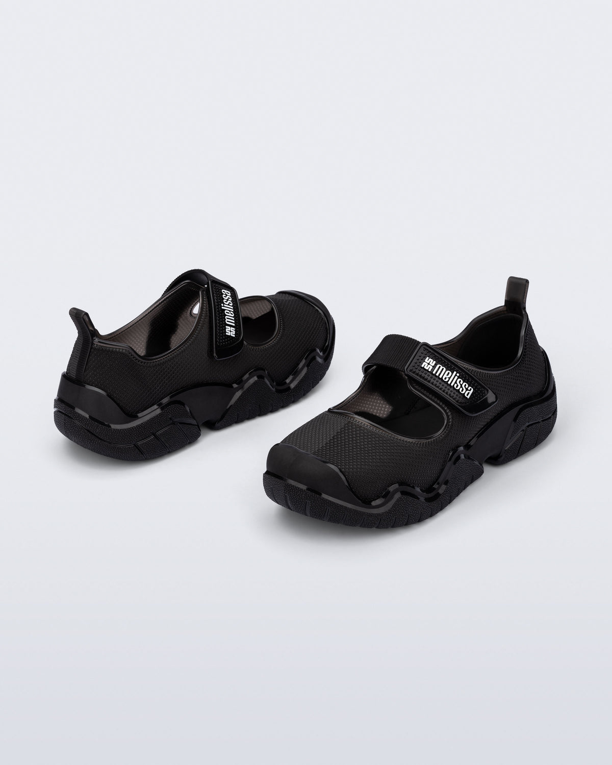 Angled view of a pair of the Melissa Sprint Ballerina flats in black with a velcro strap on a light gray background