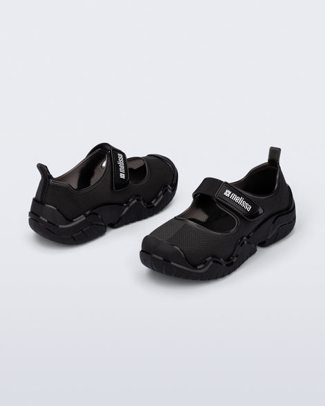 Angled view of a pair of the Melissa Sprint Ballerina flats in black with a velcro strap on a light gray background
