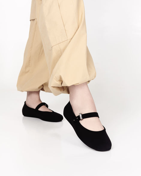 Model's legs in beige pants wearing a pair of black Soft adult flats with strap and silver buckle