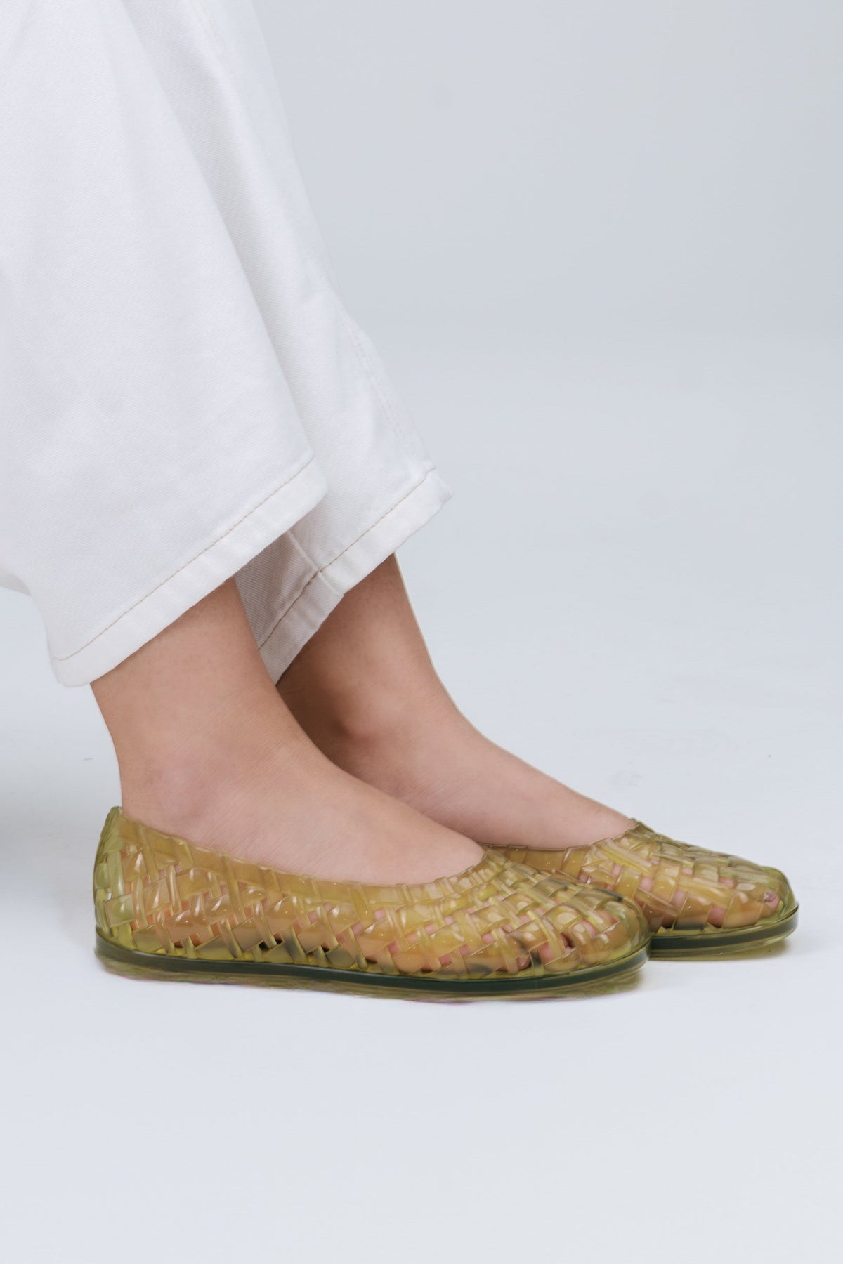 Model's legs in white pants wearing a pair of clear green Possession Ballerina flats