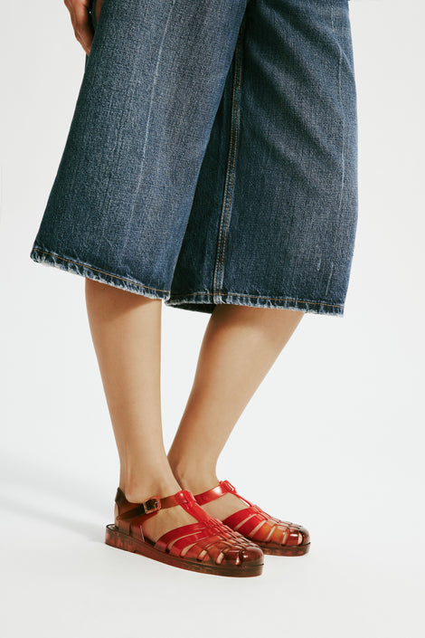 Model's legs in baggy jean shorts wearing a pair of transparent red Possession + Nodaleto fisherman sandals.