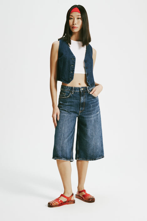 Model in a white shirt with a jean vest and jean shorts wearing a pair of transparent red Possession + Nodaleto fisherman sandals.
