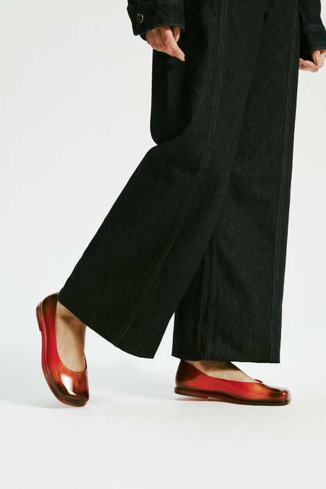 Model's legs in black baggy pants wearing a pair of transparent red Ruby + Nodaleto flats