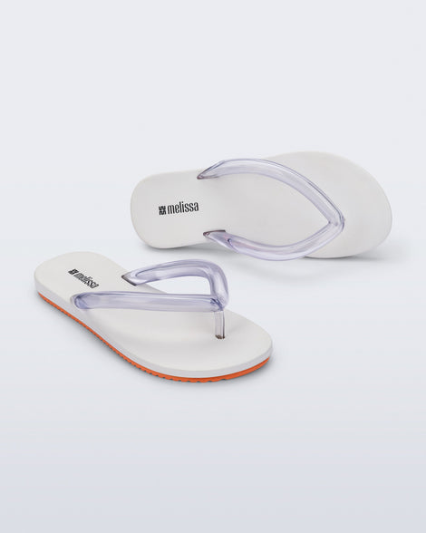 Top and angled view a pair of white Flip Flop Airflow sandal with a clear strap and orange bottom