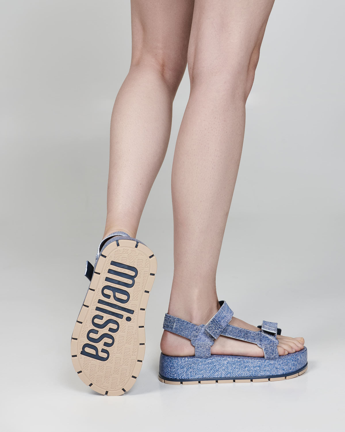 Models back legs wearing a pair of blue jean Flowing Denim platforms with one foot up showing sole of shoe with Melissa logo