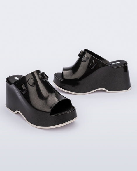 Angled and side view of a pair of metallic black Patty Stones + Undercover platform open toe mules with beige sole and stone embellishments on upper.