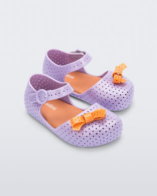 Angled view of a pair of lilac Pop baby flats with orange bow