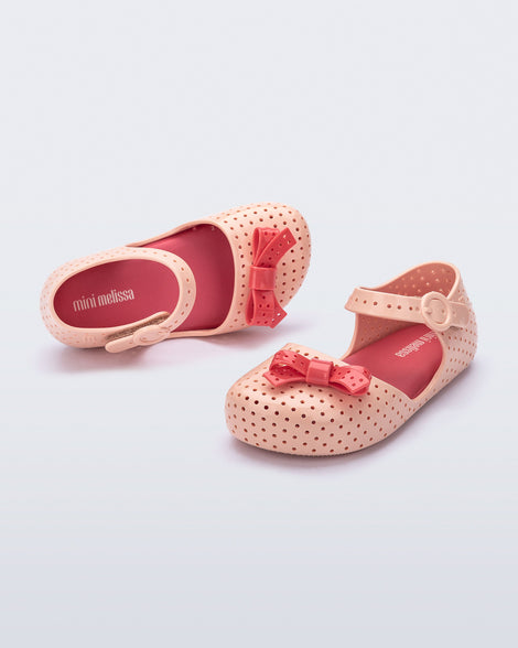 Angled and top view of a pair of light pink Pop baby flats with red bow