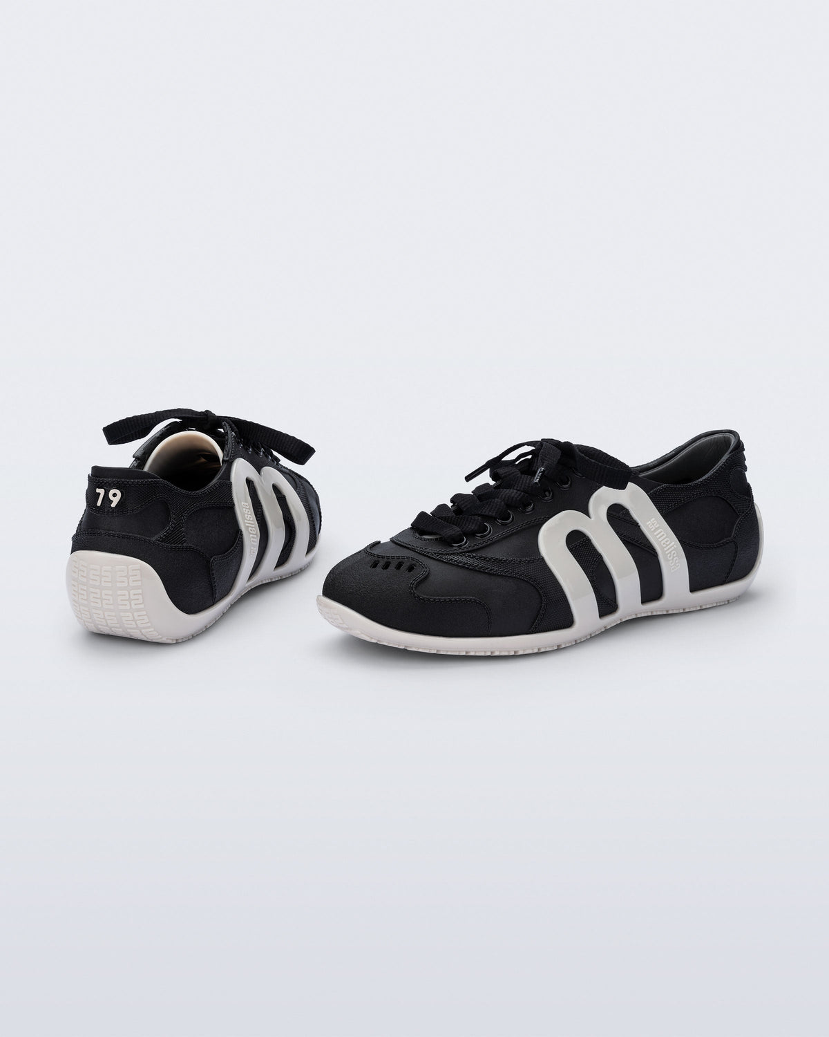 Back and side view of a pair of black Motion sneakers with white colored sole and M monogram on side and 79 on heel