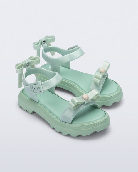 Angled view of a pair of green Town Bow sandals with bows and a pearl in the center of each bow