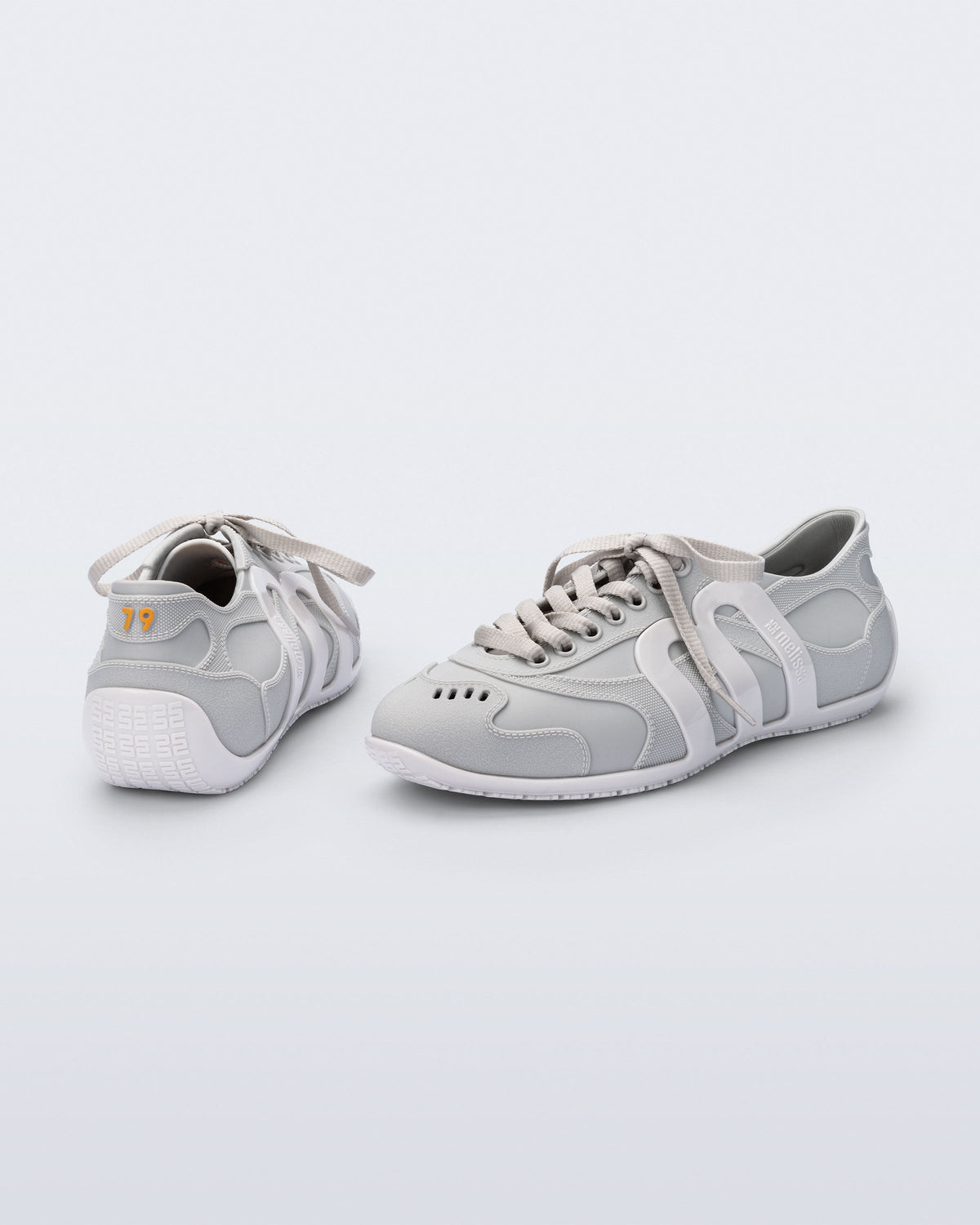 Back and side view of a pair of grey Motion sneakers with white colored sole and M monogram on side and 79 on heel