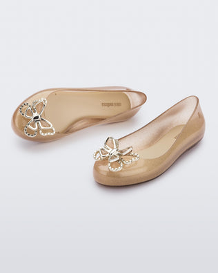 An angled front and top view of a pair of glitter beige Mini Melissa Sweet Love Butterfly flats with a gold butterfly detail on the toe