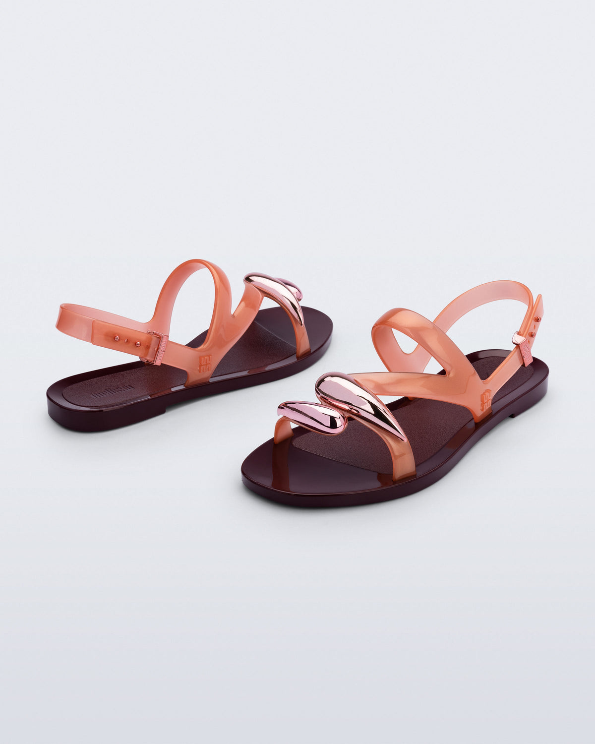 Back and angled view of a pair of orange Iris sandals with burgundy sole and rose gold upper embellishments