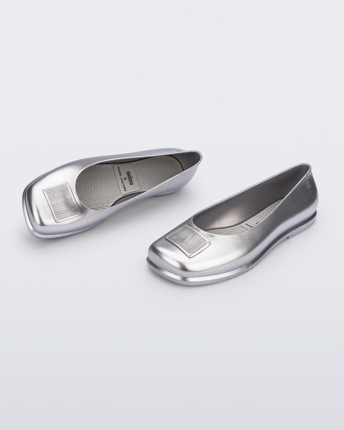 Side and angled view of a pair of metallic silver Ruby + Marc Jacobs flats