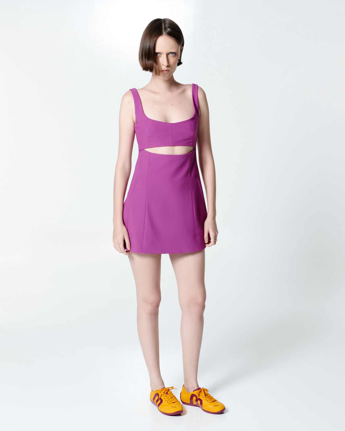 Model in pink dress wearing a pair of orange-yellow Motion sneakers with pink colored sole and M monogram