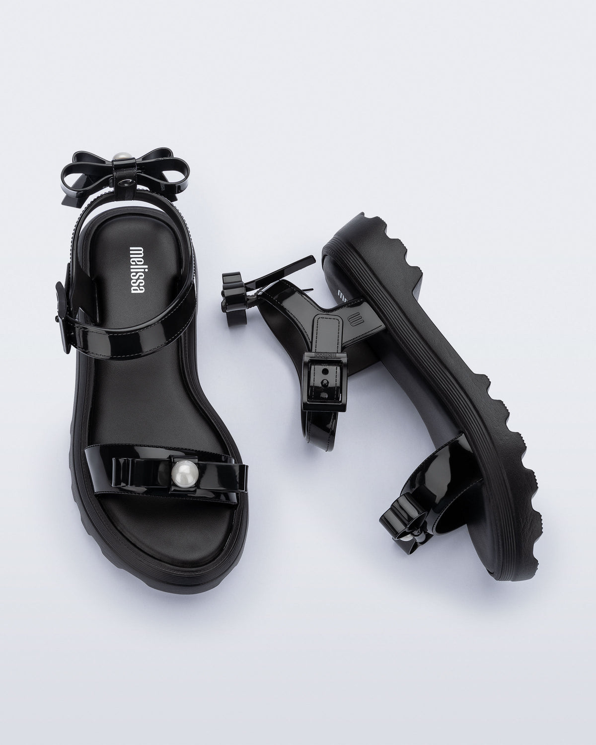 Side and top view of a pair of black Town Bow sandals with bows and a pearl in the center of each bow