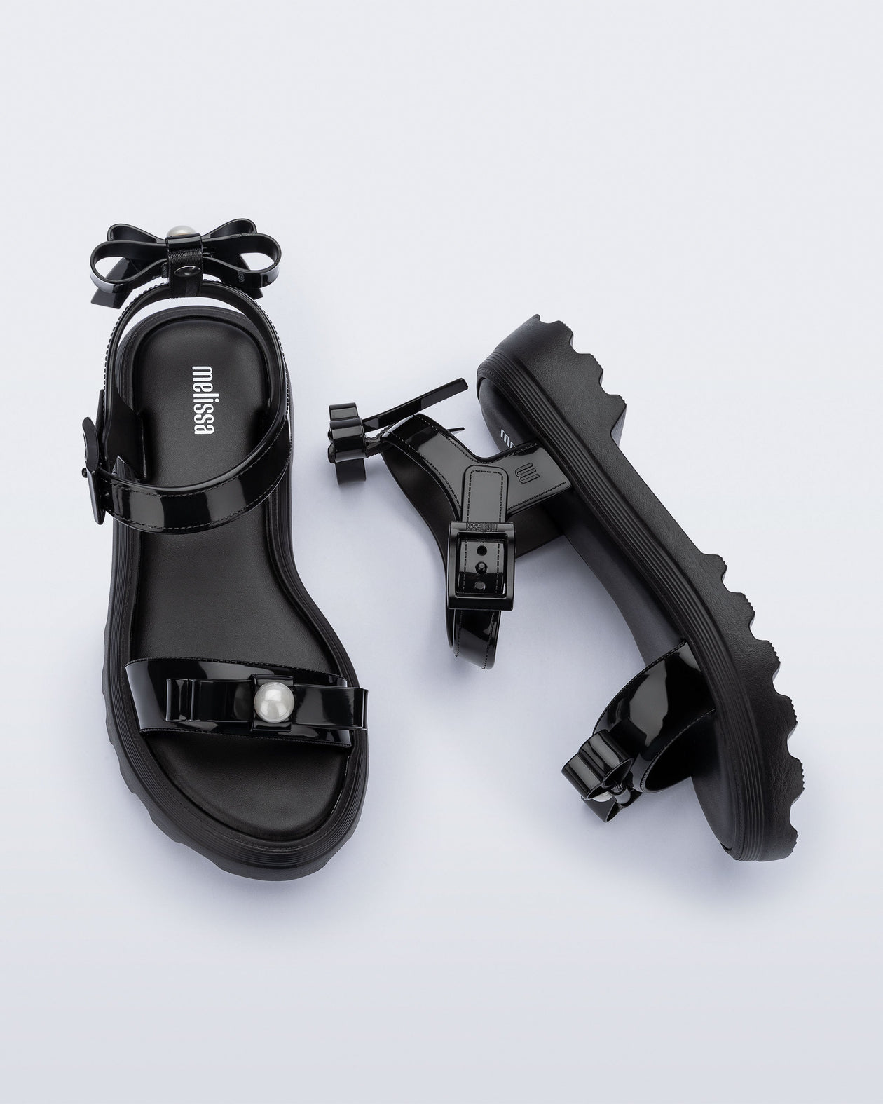 Side and top view of a pair of black Town Bow sandals with bows and a pearl in the center of each bow