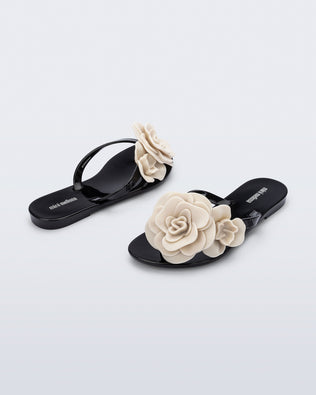 Back and angled view of a pair of black Harmonic Petals kids flip flops with beige flowers