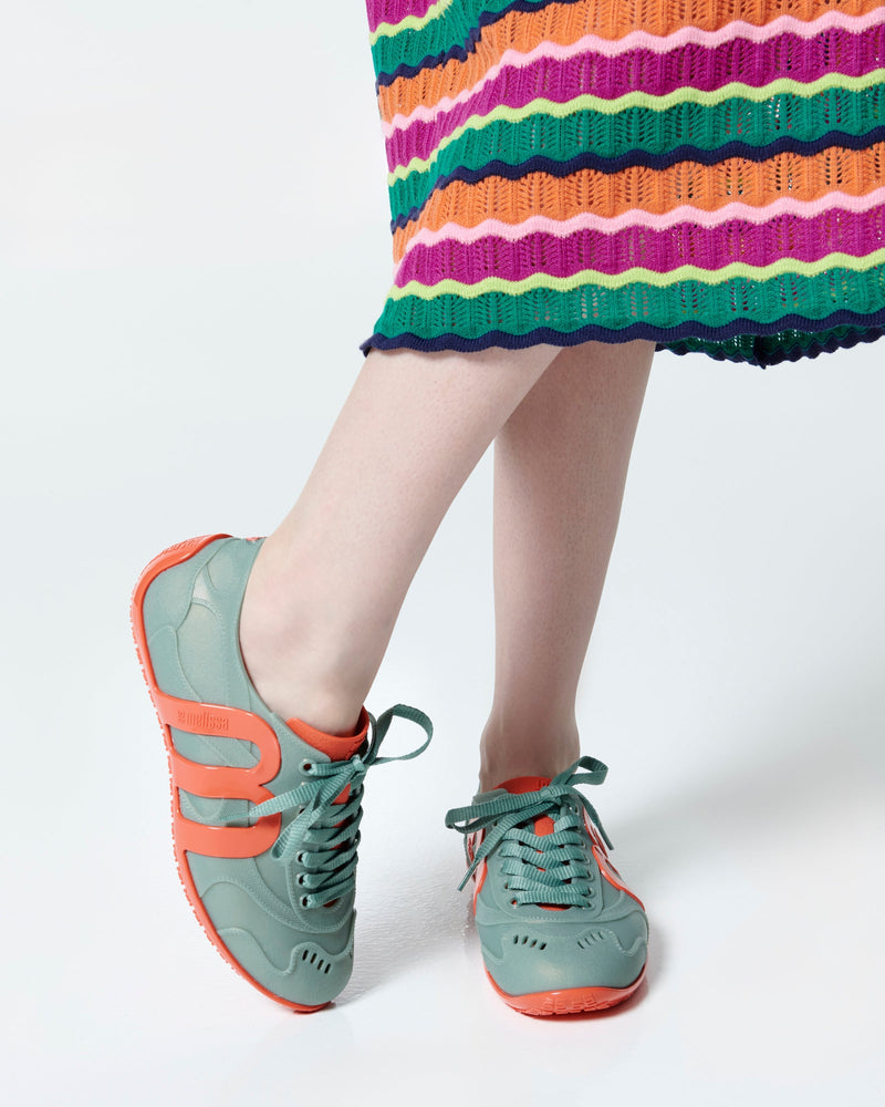 Model's legs wearing a pair of green Motion sneakers with orange colored sole and M monogram