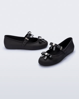 Angled view of a pair of black Soft Ballerina Bow flats with bows and a pearl in the center of each bow
