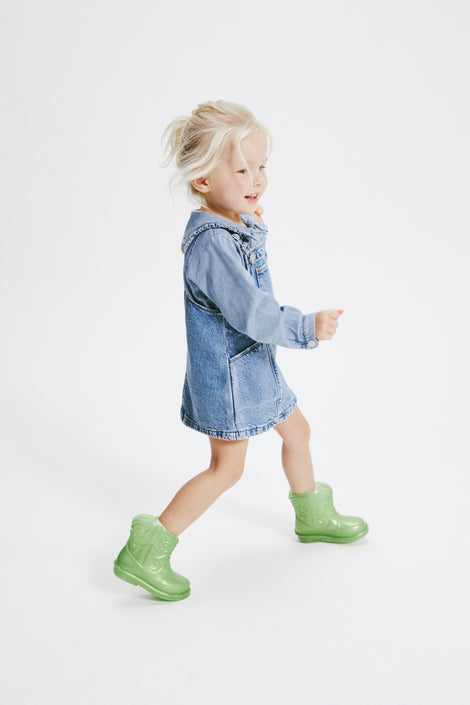 Child model running in a jean overall dress wearing a pair of pearly green Texas baby boots