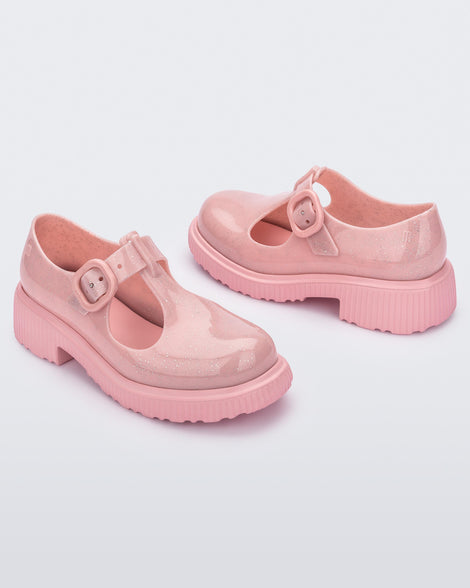 An angled front and side view of a pair of Pink Mini Melissa Jackie loafers with a pink glitter base, two cut outs, a pink buckle detail strap and pink sole.