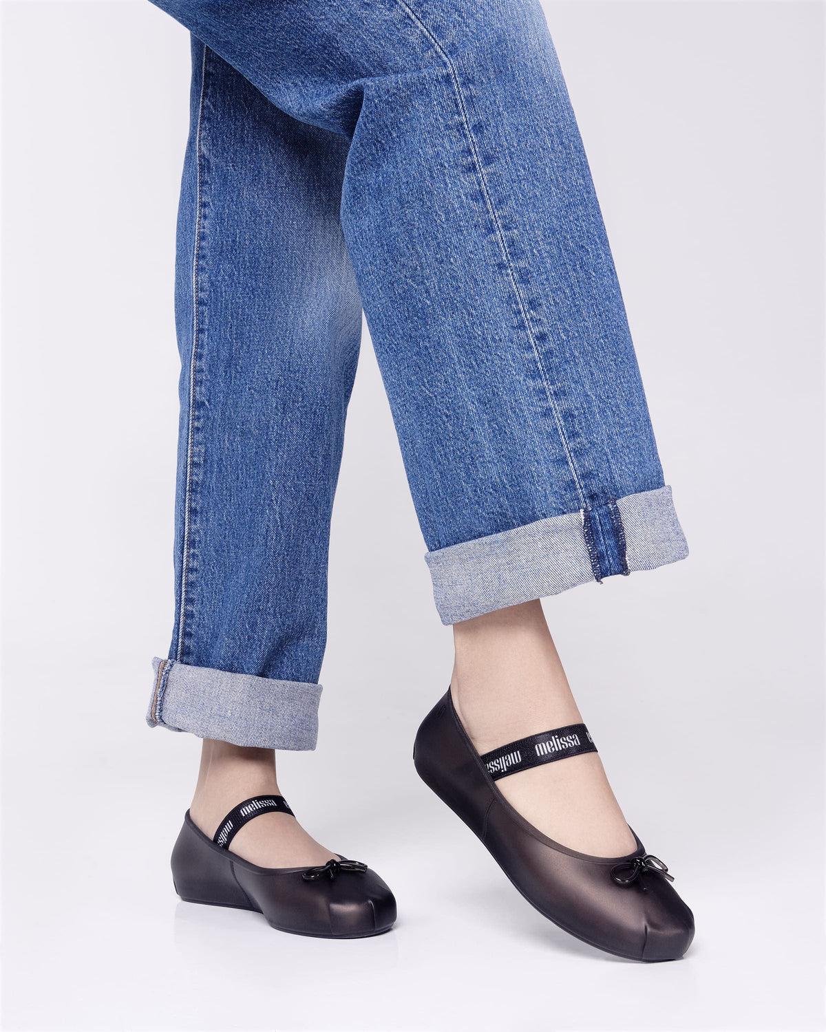 Model's legs wearing a pair of Melissa Sophie ballet flats in black with M-logo strap and bow applique