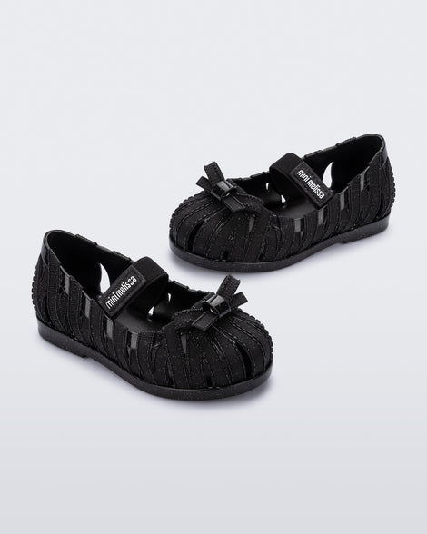 Angled view of a pair of glitter black M Lover Ballerina baby flat with bow and strap