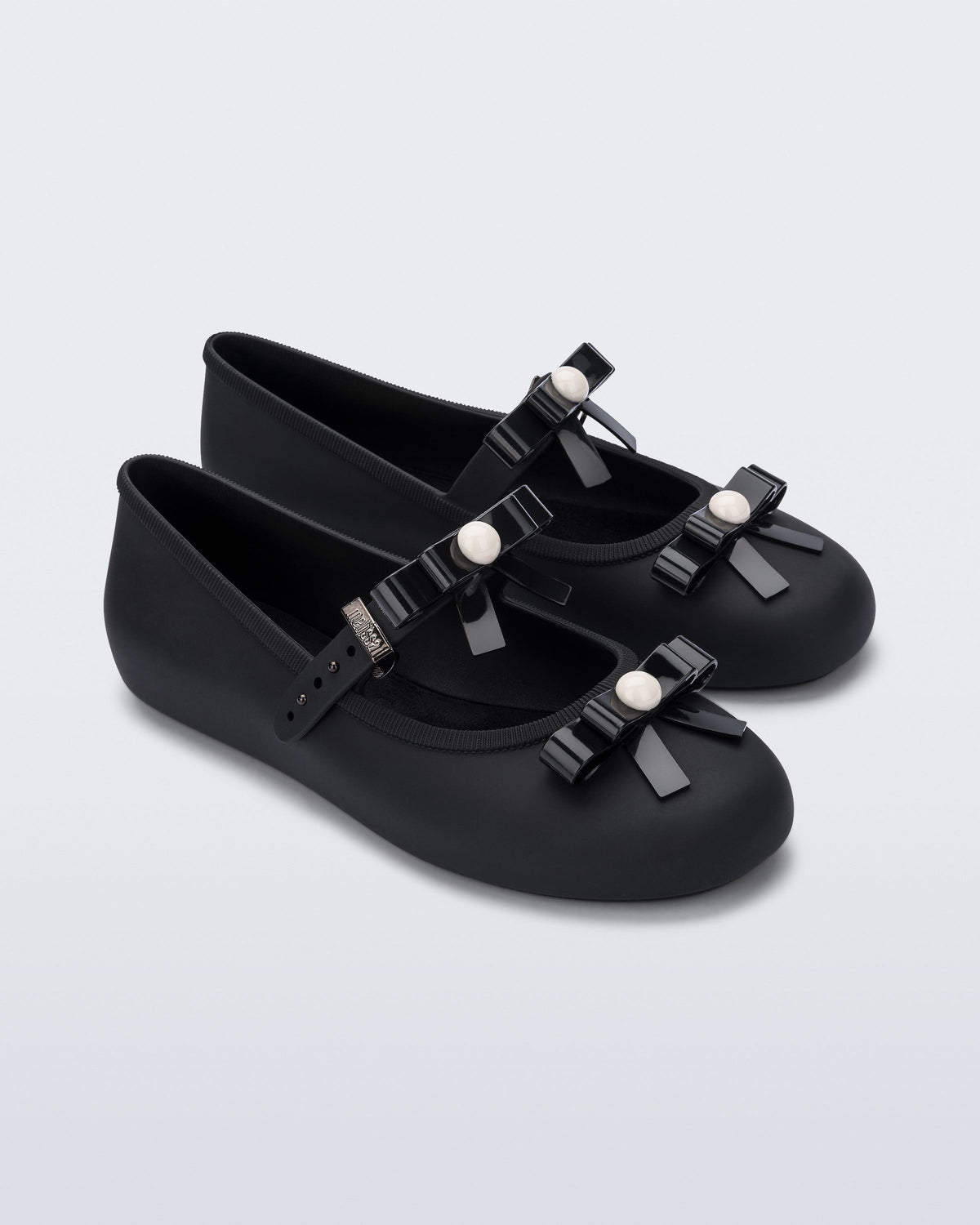 Angled view of a pair of black Soft Ballerina Bow flats with bows and a pearl in the center of each bow