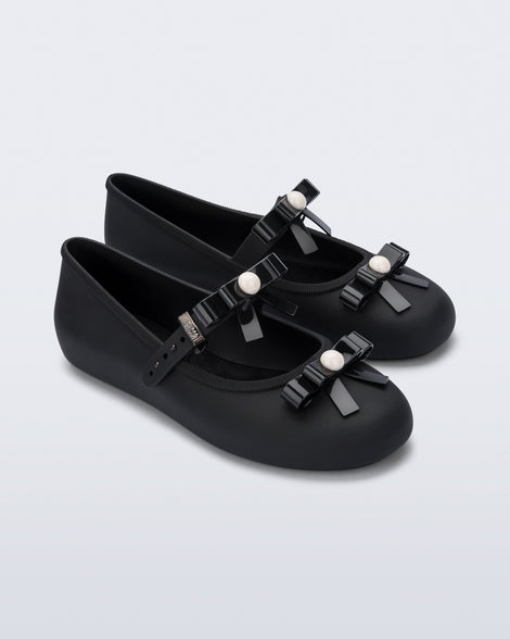 Angled view of a pair of black Soft Ballerina Bow flats with bows and a pearl in the center of each bow