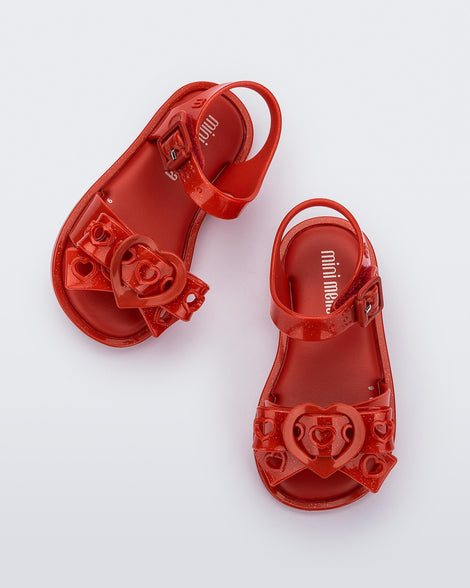 A top view of a pair of glitter red Mini Melissa Mar Sandal Heart sandals with a glitter red heart bow detail on the front strap and an ankle strap