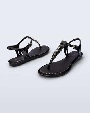 Angled view of a pair of black Solar Boho t-strap sandals with ,metallic detailing on the front strap