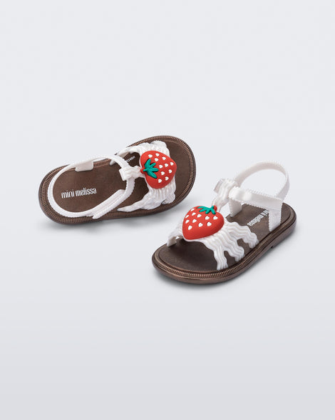 Angled view of a pair of pearly white baby Hip Sandals with red strawberry