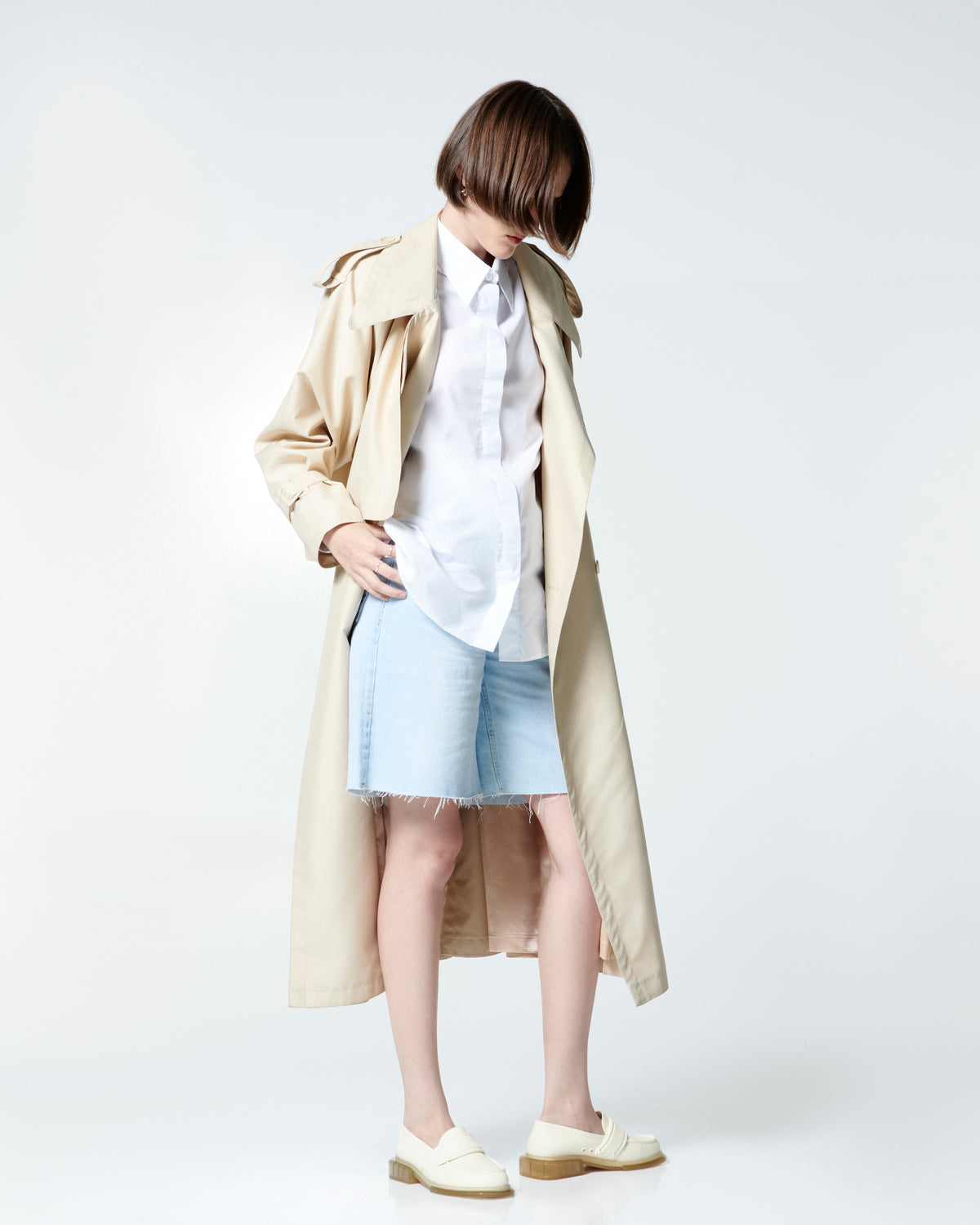Model in white button down, beige rain coat and jean shorts wearing a pair of beige Spencer loafers with clear beige soles