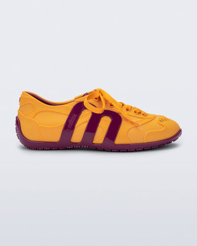 Side view of an orange-yellow Motion sneaker with pink colored sole and M monogram