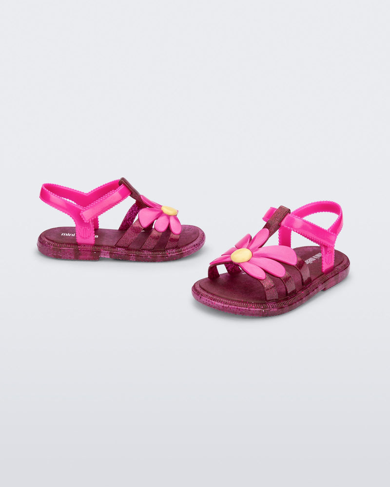 Angled view of a pair of glitter pink baby Hip Bloomy sandal with pink straps and flower