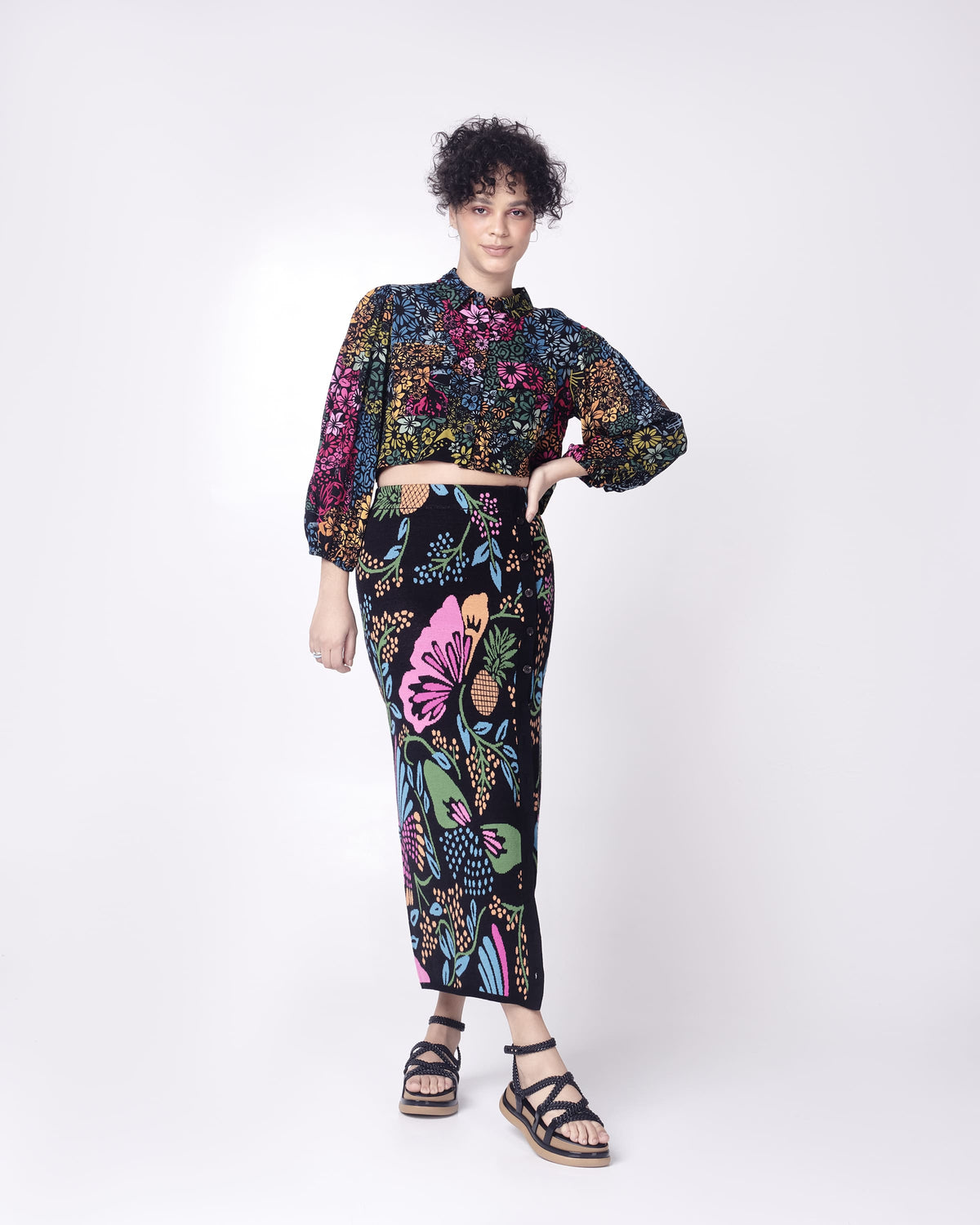 A model posing for a picture in a patterned skirt and top, wearing a pair of black Melissa Buzios platform sandals with multiple textured straps that mimic sisal braids across the front of the shoe as well as an ankle strap