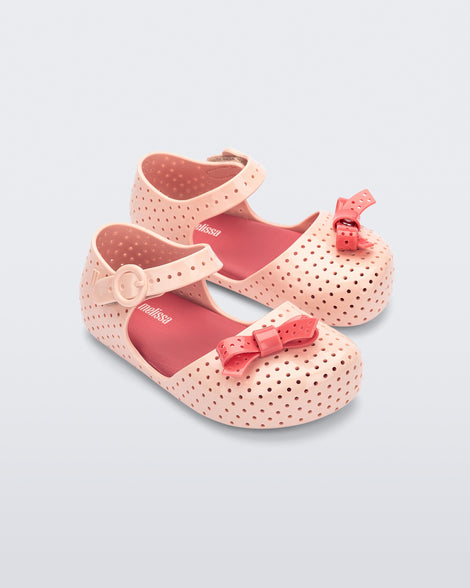 Angled view of a pair of light pink Pop baby flats with red bow