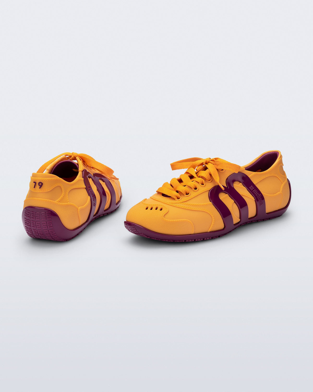 Back and side view of a pair of orange-yellow Motion sneakers with pink colored sole and M monogram on side and 79 on heel