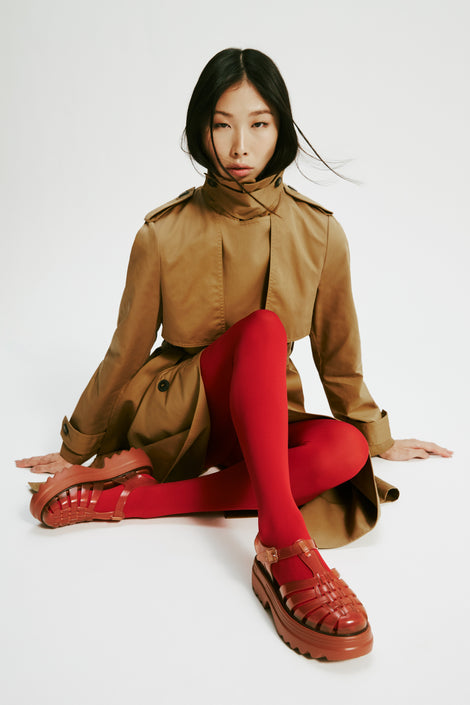 Model in a brown trench coat with red tights wearing a pair of transparent brown Possession Platform II fisherman sandals.
