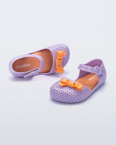 Angled and top view of a pair of lilac Pop baby flats with orange bow
