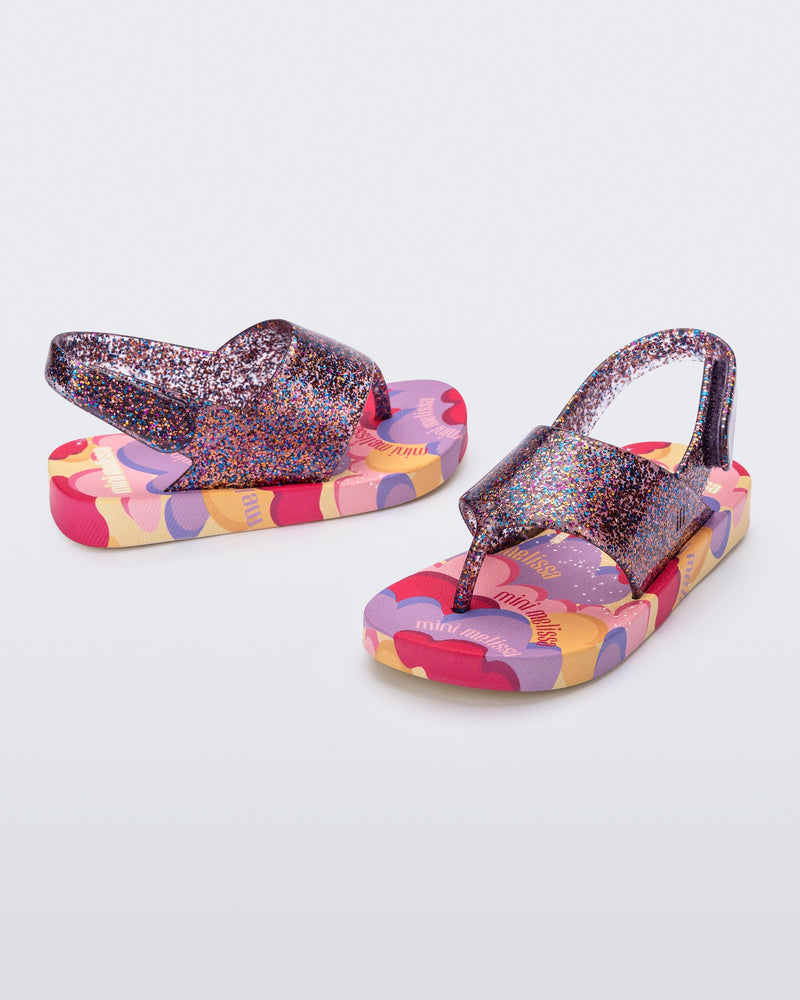 Angled view of a pair of lilac glitter Shiny baby sandals with multicolor sole