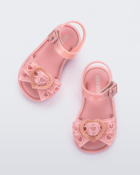 A top view of a pair of glitter pink Mini Melissa Mar Sandal Heart sandals with a glitter pink heart bow detail on the front strap and an ankle strap