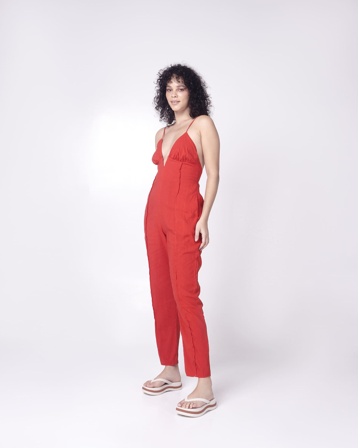 A model posing for a picture in a red romper, wearing a pair of beige/brown Melissa Leblon platform flip flops with details that mimic sisal braids on the sole and strap