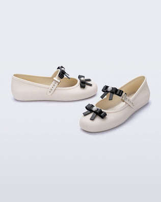 Angled view of a pair of beige Soft Ballerina Bow flats with black bows and a pearl in the center of each bow
