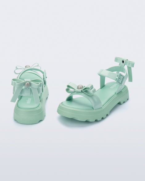 Angled and back view of a pair of green Town Bow sandals with bows and a pearl in the center of each bow